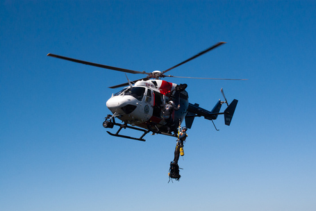 Heli an dem mehrere Retter an seilen gesichert plus deren Rucksäcke hängen.
